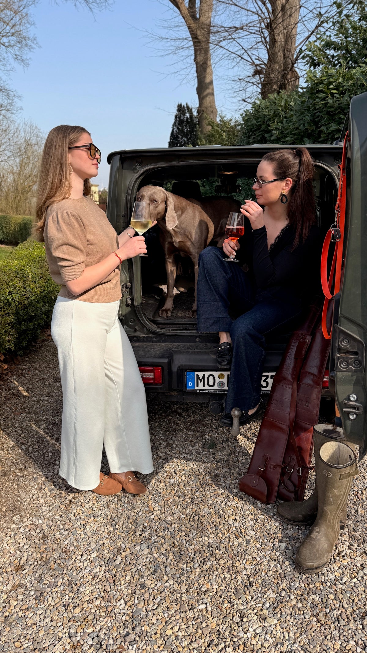 Zwei Freundinnen mit Weißwein und Rosé am Geländewagen, ein Weimaraner schaut aus dem Kofferraum